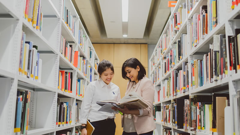 lecturer and student look at books among the shelves in JHBB library