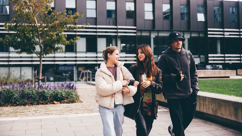 Three students walking and talking to each other outside Clerici building