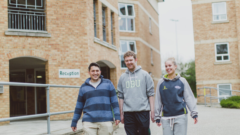 Three students smiling whilst walking through outdoor hall grounds.