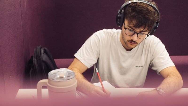 Student wearing headphones and writing in a notepad