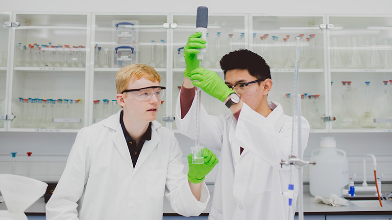Two students in a lab conducting an experiement with a large syringe