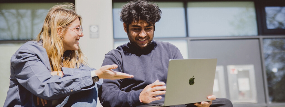Two students discussing copy on a laptop screen