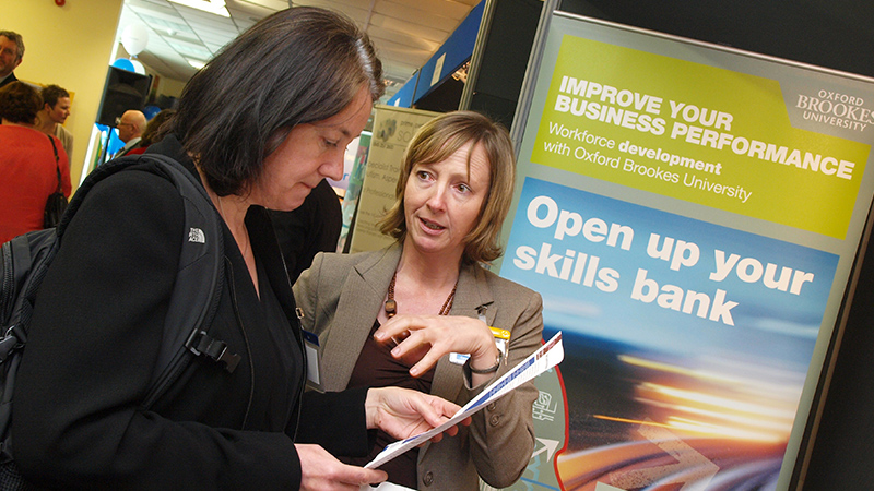 Two people in front of an 'Open up your skills bank' poster