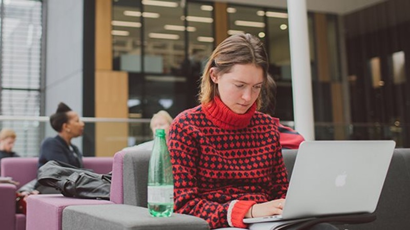 student wearing red jumper working on laptop in JHB Library