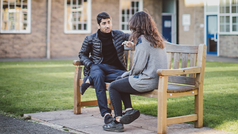 Male and female student sitting on a bench talking