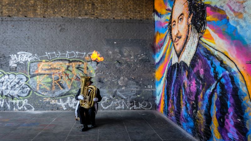 man playing tuba next to mural of Shakespeare