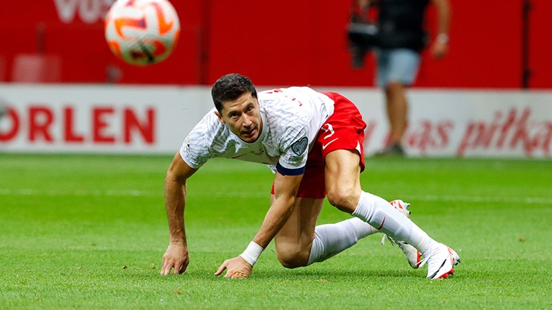 A footballer crouching on football pitch with ball mid-air