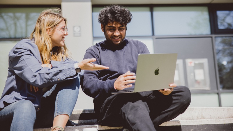 two students discussing while looking at laptop screen