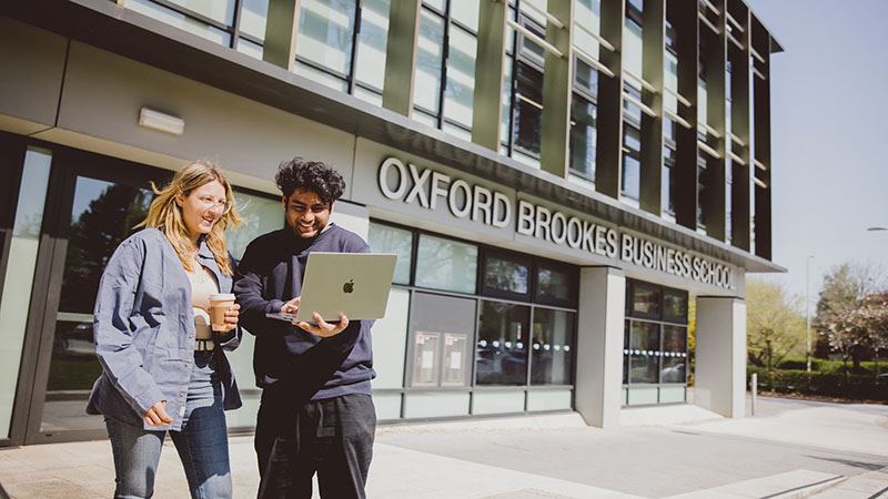 Two students on laptop outside Oxford Brookes Business School