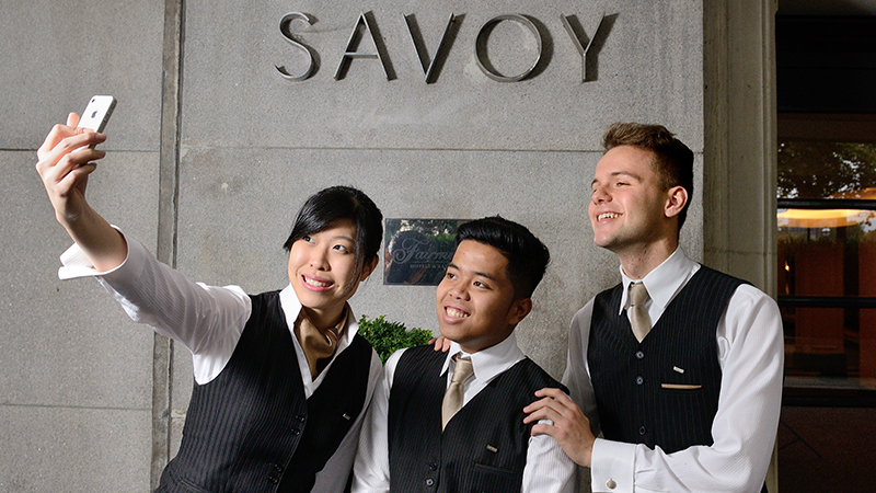 Three people standing in front of a 'Savoy' sign taking a photo of themselves