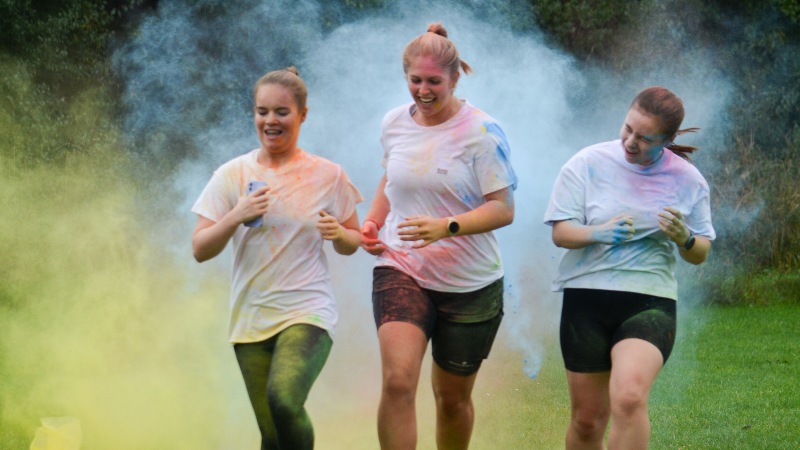 Three students in white t shirts running covered in powder paint