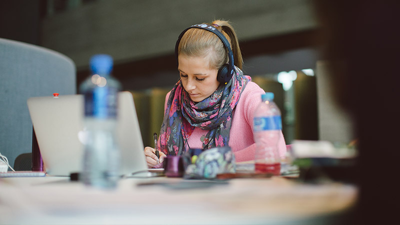 Female student working on laptop with headphones in