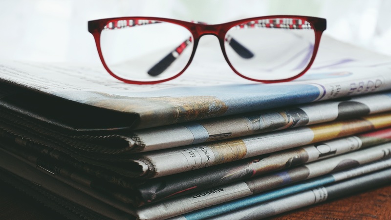 Pair of red-framed glasses on top of stack of newspapers