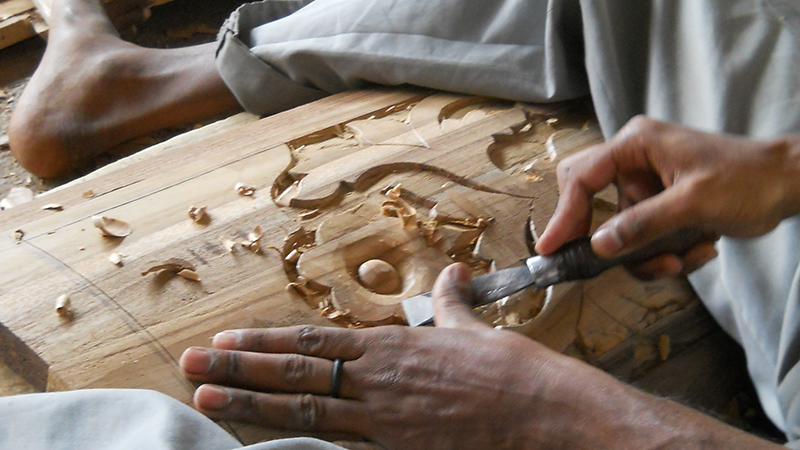 Man carving wood between his legs