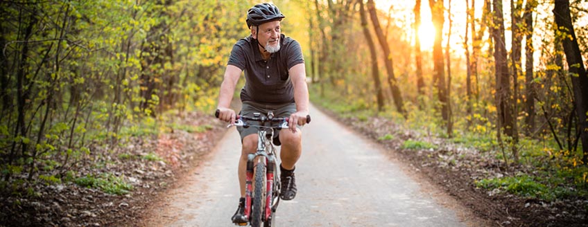 older man cycling through a forest 