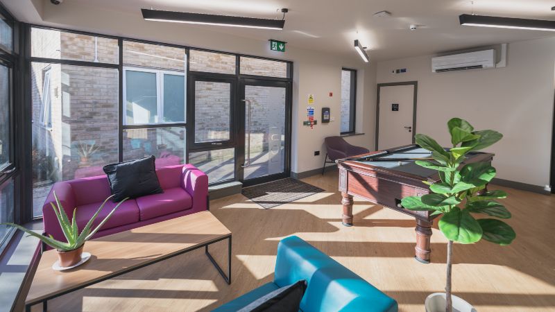Social space with large windows, sofa seating, coffee table, plants and pool table.